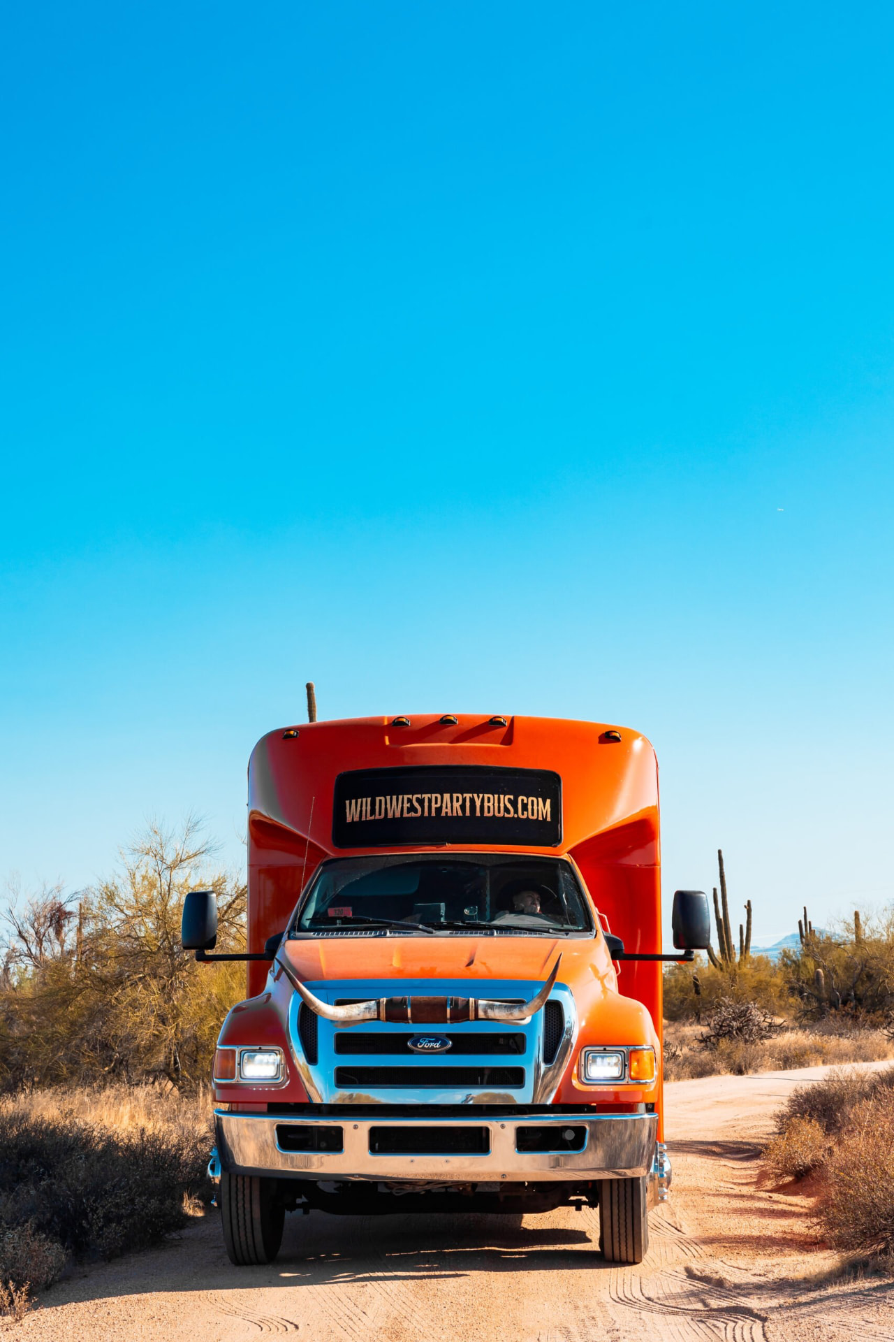 Front view of the bus on a desert road with the giant bull horns mounted across the grille