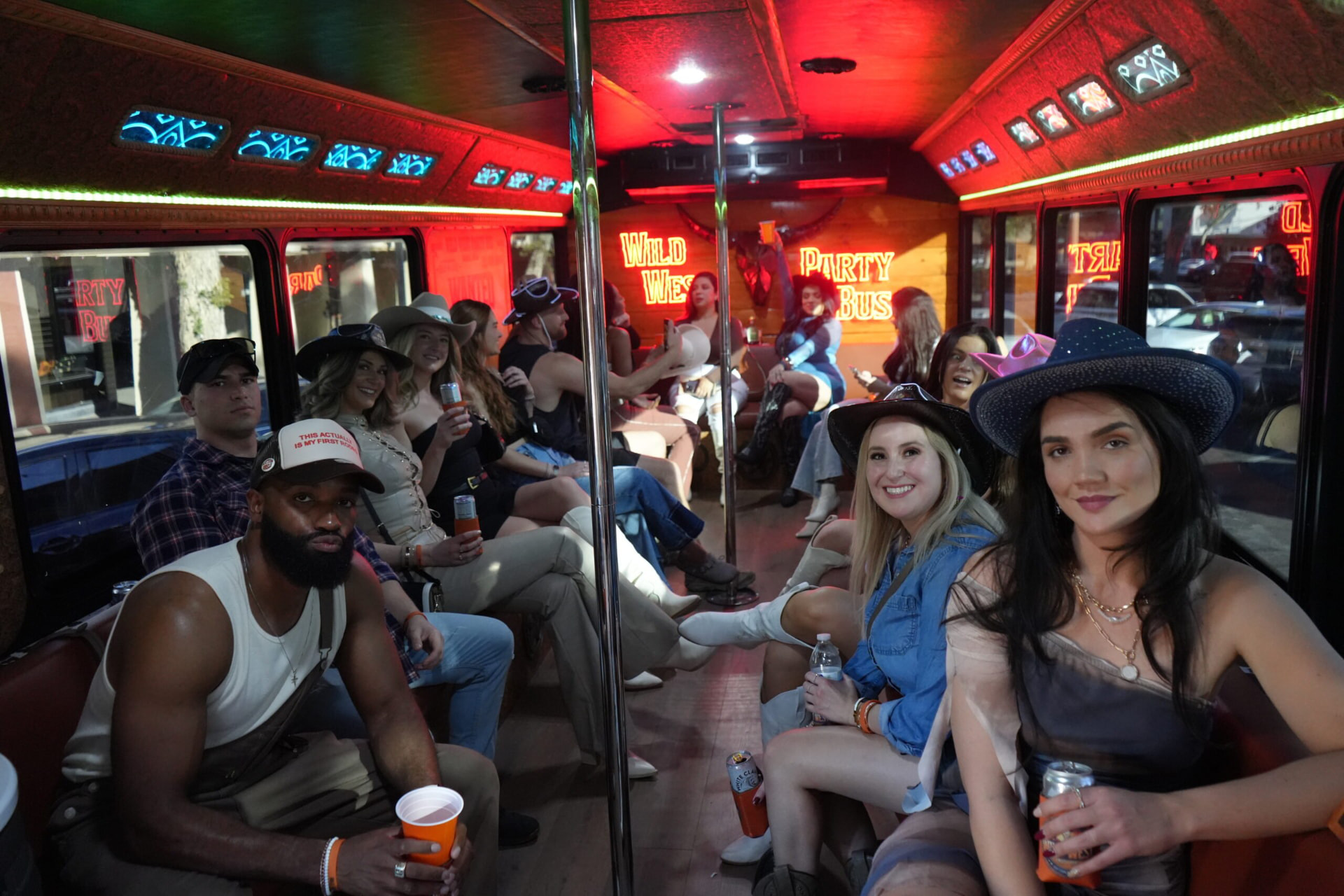 Inside the party bus: guests seated along wraparound leather benches under neon Wild West Party Bus signs